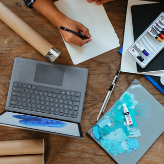 Artist's workspace with a laptop, notebook, and painting supplies