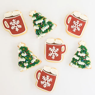 Holiday sugar cookies decorated as Christmas trees and mugs of hot cocoa.